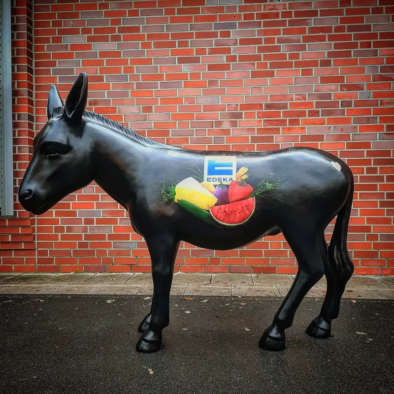 Schwarze Esel-Skulptur vor einer Klinkerwand, auf der Flanke das EDEKA-Logo mit Melone, Paprika und Trauben