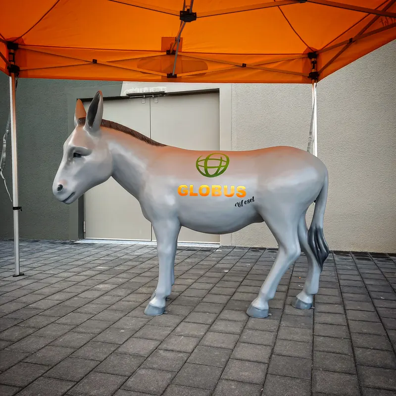 Silbergraue Esel-Skulptur mit grünem Globus-Logo und dem Schriftzug Globus Wesel, unter einem orangen Pavillon