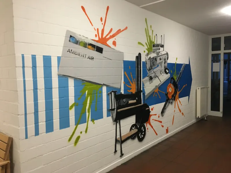Flur mit weißer Ziegelwand, blauen Streifen, bunten Farbspritzern und gesprühten Technikgeräten