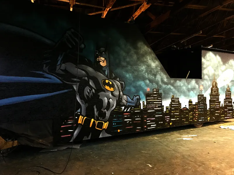 Große Wand in einer Halle mit Comicfigur im Wolkenhimmel über einer beleuchteten Hochhaus-Skyline