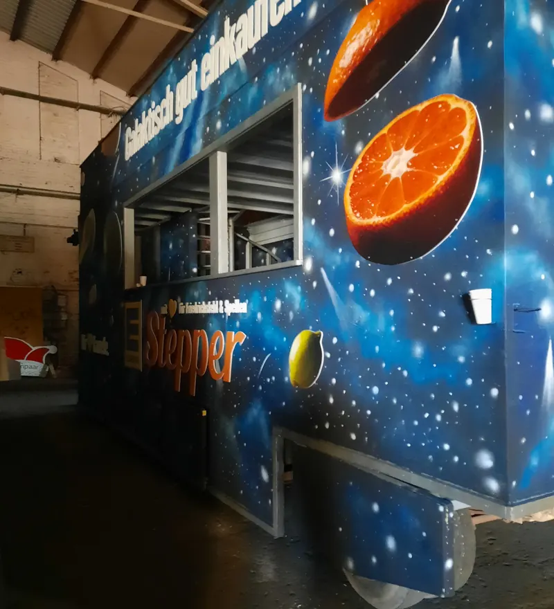 Verkaufswagen mit Weltraum-Graffiti: aufgeschnittene Orangen und Zitrusfrüchte vor blauem Sternenhimmel