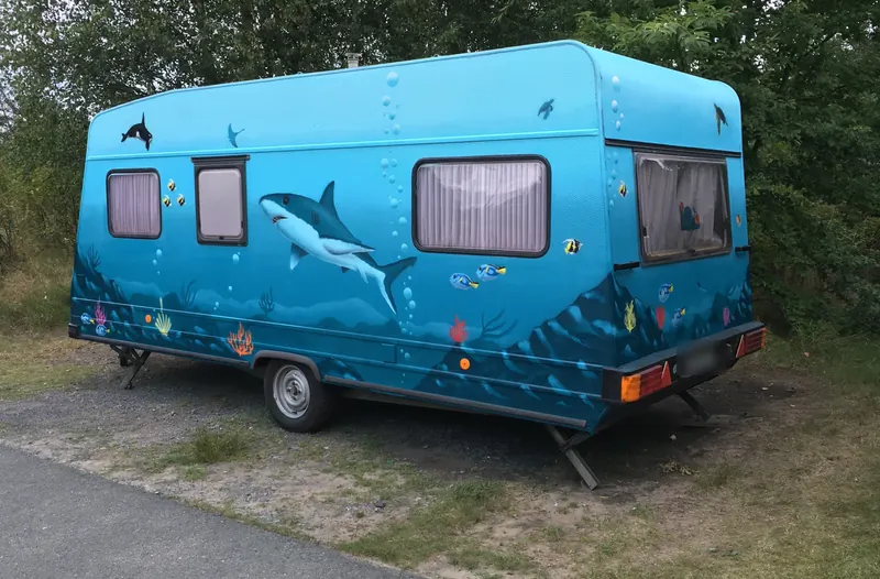 Türkis gestalteter Wohnwagen mit Unterwassermotiv: weißer Hai, Orca, bunte Fische und Korallen