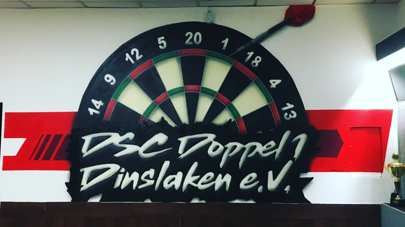 Wandbild im Vereinsheim eines Dartclubs: Dartscheibe mit Vereinsname und rotem Streifen